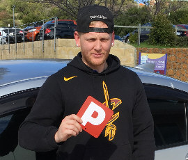 Male student standing by driving school vehicle holding his P plate