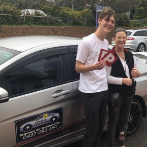 Young male student standing next to driving school car with his driving instructor, showing both P plates after passing driving test